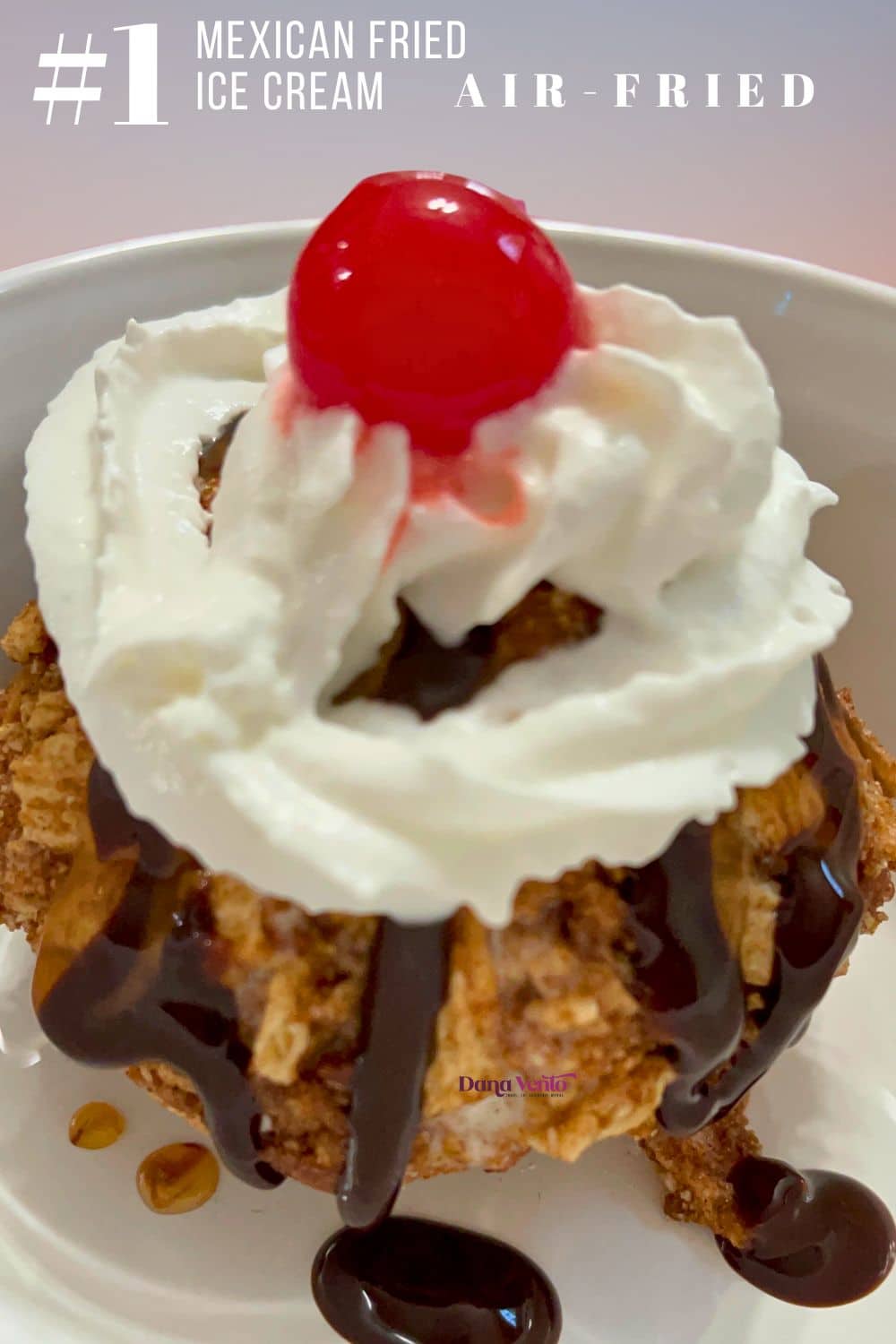 A golden Air Fried Mexican Fried Ice Cream ball topped with caramel chocolate syrup whipped cream and a cherry