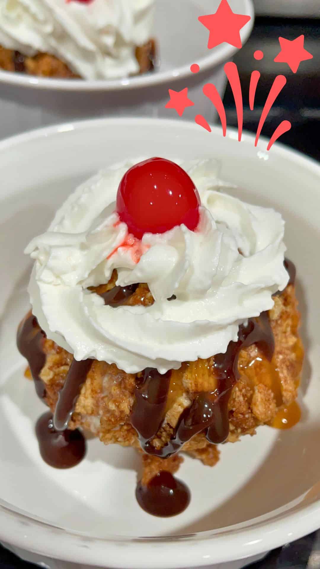 A vibrant cherry topping an Air-Fried Mexican Fried Ice Cream ball surrounded by whipped cream and caramel sauce