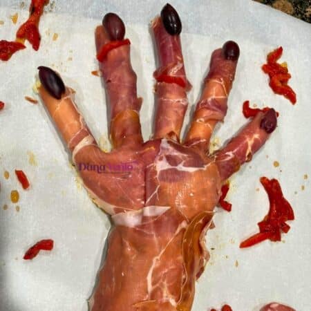 Edible amputated hand appetizer for Halloween with Kalamata nails and cuts of roasted red peppers for blood
