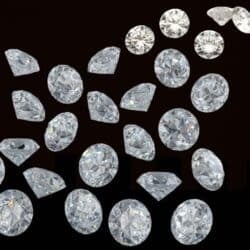 Loose moissanite stones of varying cuts and brilliance scattered on a black background, showcasing intense sparkle and light refraction.